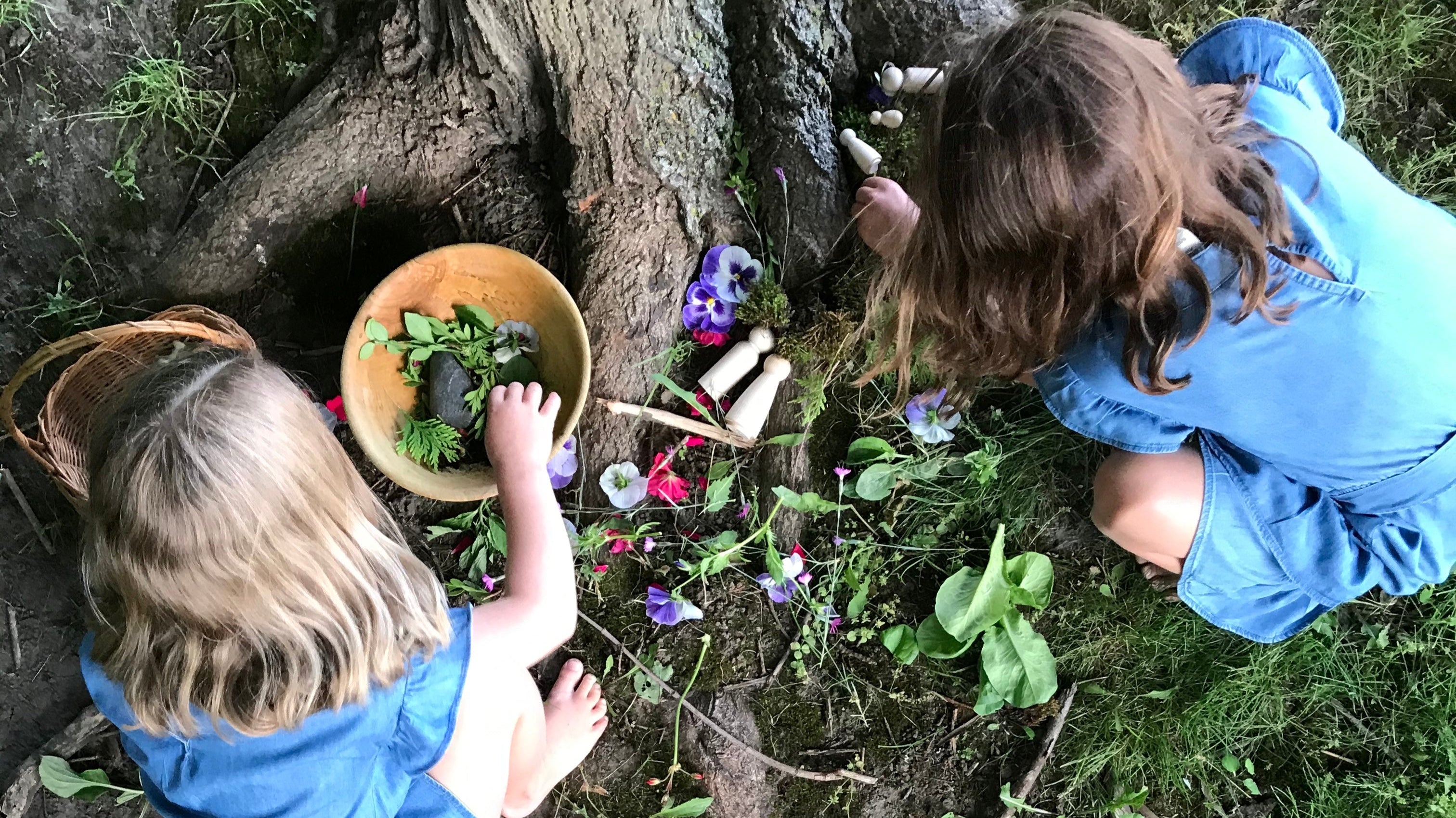Two girls forage for nature craft materials in the woods.